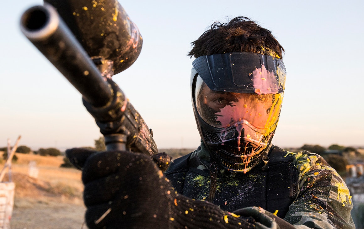 A man holding a paintball gun wearing a face shield